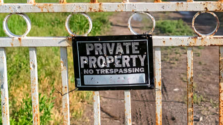 Panorama frame Private Property sign on an old rusty white gate locked with chain and padlock. A dirt road leads to the lake with view of mountain against cloudy sky.の写真素材