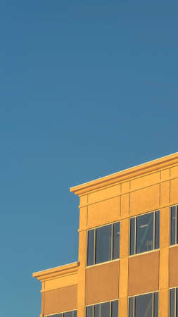 Vertical frame Modern building exterior viewed on a sunny day against clear blue sky. Facade of a sunlit commercial building with large glass windows.の写真素材