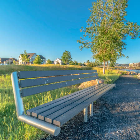 Square Bench at the shore of a lake with homes and buildings background on a sunny dayの写真素材