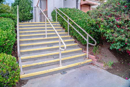 Cement entrance steps with yellow warning painted on the treads viewed from below with hand rails