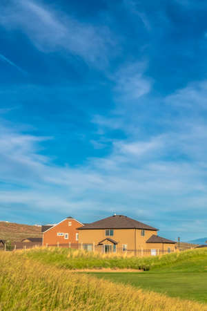 Green grasses of golf course with houses and mountain in the scenic background. Golfing and residential area in the suburbs with cloudy blue sky overhead.の写真素材