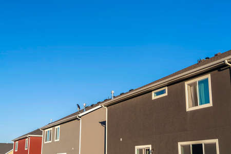 Houses with close up view of exterior walls windows and roofs against blue sky. Homes with hip and...