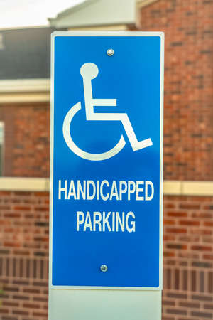 Close up of Handicapped Parking sign against blurred red brick wall of church. Blue and white sign with an icon of a person on a wheelchair at the parking lot.の写真素材