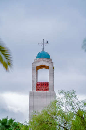 Bell tower of a small church above leafy green trees topped with a small blue dome and crossの写真素材