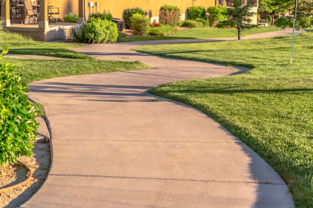 Close up of narrow paved pathway winding through lush grasses on a sunny day. The road passes...