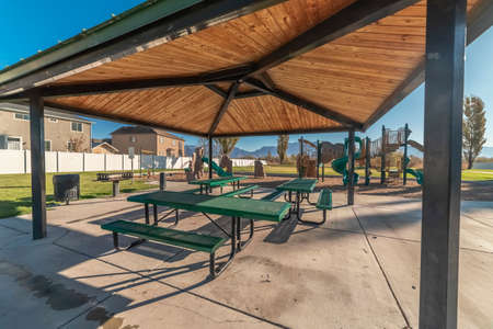 Empty green tables and benches in an urban park covered by wooden roofing on a paved base in close upの写真素材
