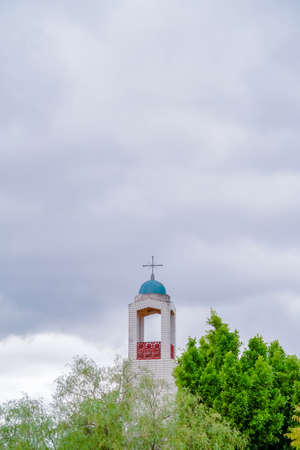 Bell Tower of a church rising above green trees against a cloudy grey sky with copy spaceの写真素材