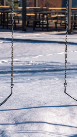 Vertical Two swings on chains in a winter playground outdoors with fresh white snow on the groundの写真素材