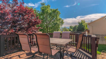 Pano Sunlight beaming down on the wooden balcony of a home with table and chairs. Stairs parallel to...
