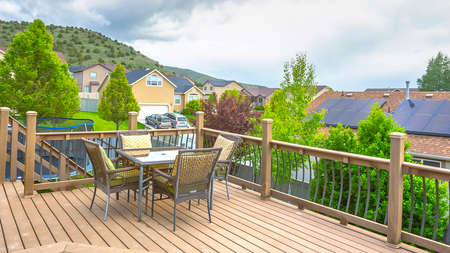 Pano Deck overlooking solar panels on roof of home against mountain and cloudy sky. The deck has wooden floor, furniture, and stairs that leads down to the yard.の写真素材