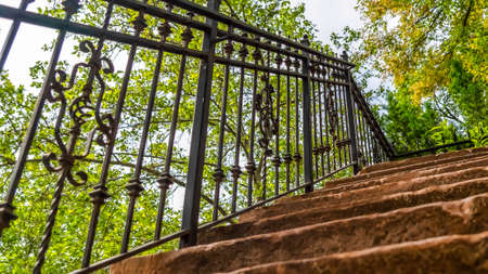 Pano frame Close up of staircase with stone treads and metal railing against leaves and sky. Outdoor stairway against a stone wall viewed on a sunny day.の写真素材