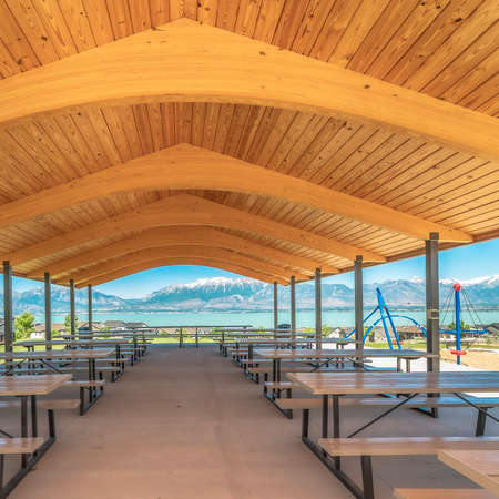 Square frame Pavilion with brown wooden ceiling overlooking lake and snow capped mountain. Colorful children's playground and houses can also be seen from the picnic area.の写真素材