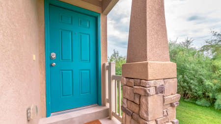 Pano frame Blue green door of a home with doormat railing and stone pillar at the entrance. Yard...
