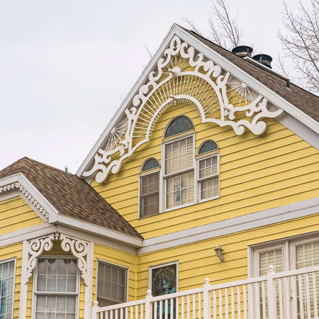 Square Home in Park City with pastel yellow wall and balconies with white railings. The lovely house also features bay windows and arched attic windows.の写真素材