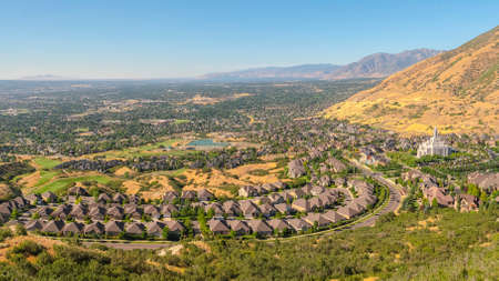 Pano Scenic view of the suburb in Salt Lake City Utah surrounded by mountains. Stunning landscape with residential houses and iconic temple under blue sky.の写真素材
