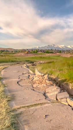 Vertical frame Damaged road with view of homes and snow capped mountain against cloudy skyの写真素材