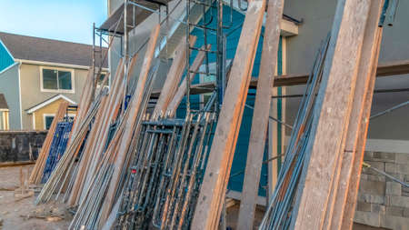 Pano Construction materials and scaffolding against brick and concrete wall of home. Close up view of scaffolds and steel poles outside of a house on a sunny day.の写真素材