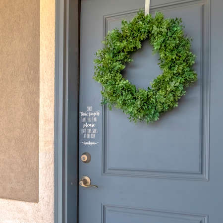 Square frame Home exetrior with close up on blue gray front door decorated with green wreath....