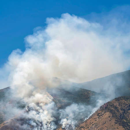 Square frame Aerial view of mountain with white smoke from wild forest fire on a sunny day. Nature...