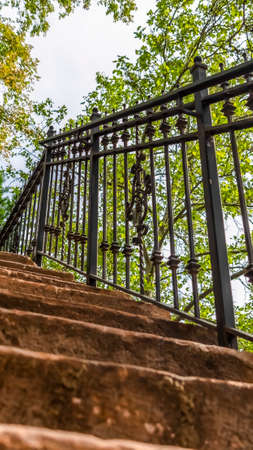 Vertical Close up of staircase with stone treads and metal railing against leaves and sky. Outdoor stairway against a stone wall viewed on a sunny day.の写真素材