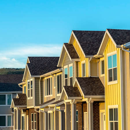 Square frame Townhomes with wood and brick exterior wall against mountain and blue sky. Steps flanked by square columns leads to the white front doors.の写真素材
