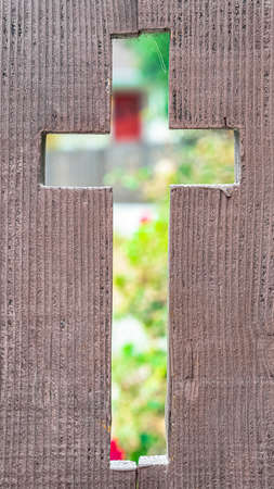 Vertical frame Cross shaped opening in a rustic wooden fence with a view through to flowers in a garden in a close up viewの写真素材