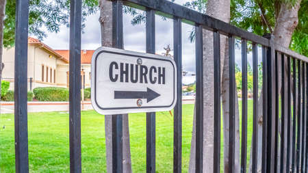 Panorama frame Church sign with arrow outdoors on a wrought iron railing or fence lined with young treesの写真素材