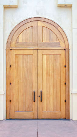 Vertical Double arched wooden entrance door in a cream colored exterior wall with paved walkway