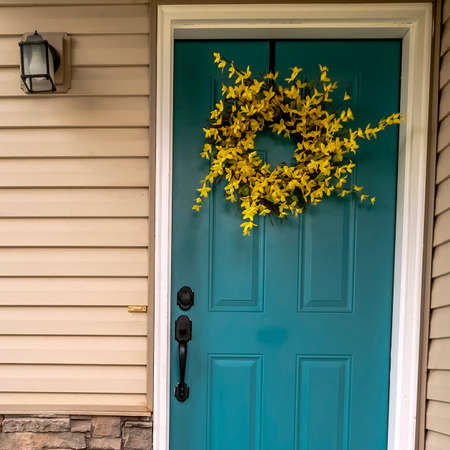 Square frame Wooden blue entrance door with floral wreath on a small covered porch of an urban house
