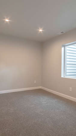 Vertical frame Empty modern room interior with down lights and neutral colored walls in a receding...