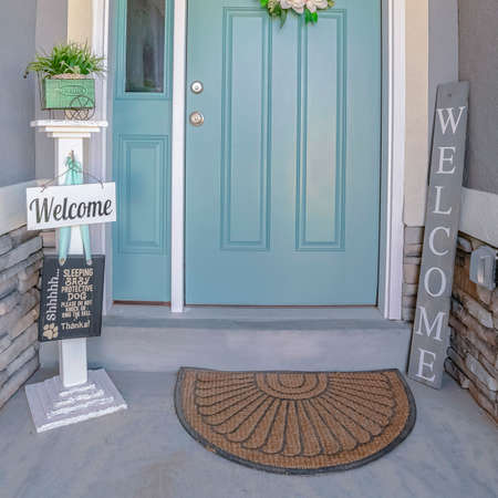 Square frame House with green front door with floral wreath and a welcome sign on either side under a covered porchの写真素材