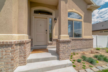 Home entrance with steps white front door sidelight arched windows and yard. Architectural style of a house with rustic concrete wall and stone brick accents.の写真素材