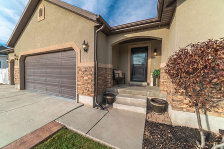Covered house entrance with glass door adjacent to a garage with flowerbed and shrubs in the foregroundの写真素材