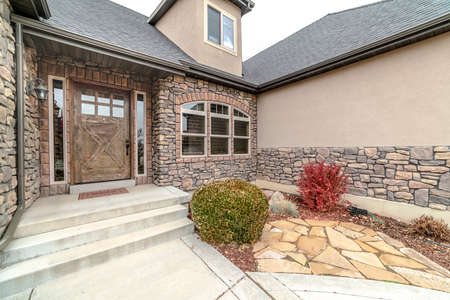 Modern urban home with feature stone brick wall, arched window and wooden entrance door with glassの写真素材