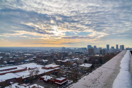 Elevated rooftop view of snow in Salt Lake City, Utah in winter covering the rooftops of the buildings at sunrise or sunset with a glow in the skyの写真素材