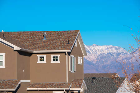 Traditional American two story house with brown facade and soft roof, viewed from low angle against mountain backgroundの写真素材