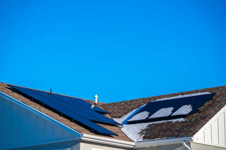 Fresh winter snow and photovoltaic solar panels on a roof under a blue sunny sky for green renewable...