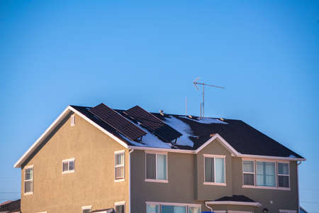 Two angled solar panels on a double storey house roof providing renewable energy with remnants of winter snow under a sunny blue skyの写真素材