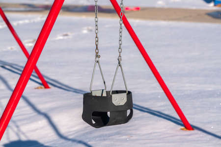 Close up on a kids swing with bright red metal supports in thick pristine white winter snow conceptual of the seasonの写真素材