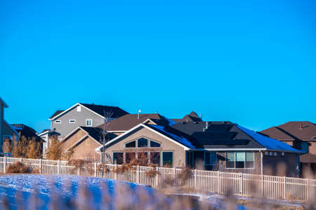 American house with solar panels on the roof during winter season, viewed from distance on sunny day against clear blue skyの写真素材