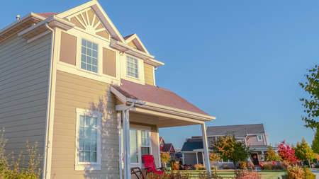 Panorama frame Low angle view of wooden beige colored house with colorful red chair on an open covered porch in a neat landscaped gardenの写真素材