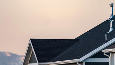 Panorama frame Cropped image of traditional American house with dark roof and snowy mountain peak...