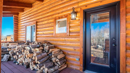 Panorama Log cabin with stacked firewood on the porch outside a glass panel front doorの写真素材