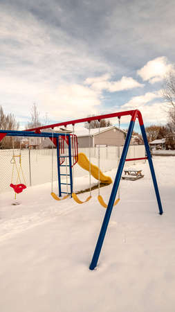 Vertical Kids playground in winter snow with swings, climbing frames and a slide with tracks in the fresh powderの写真素材