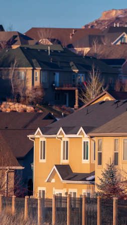 Vertical Selective focus of cozy brown houses on the hills in American town and bare trees in winter season and long fencing in foregroundの写真素材