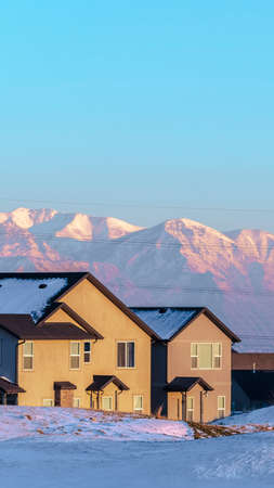 Vertical Houses on the shore of Utah Lake in winter with snow and the ground and snow-capped mountain peaks behind at sunsetの写真素材