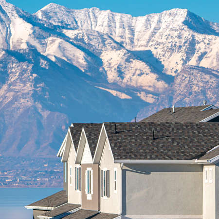 Square frame Majestic snow capped mountains above Utah Valley in winter viewed past houses in an estate on the shore of the Lakeの写真素材