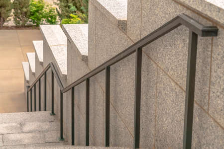 Outdoor staircase of a building with gray metal handrails against side wall. The stairway leads to a...