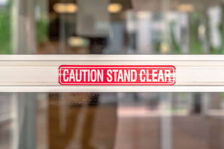 Caution Stand Clear sign on the metal plate of the glass door of a building. Warning signage at the...