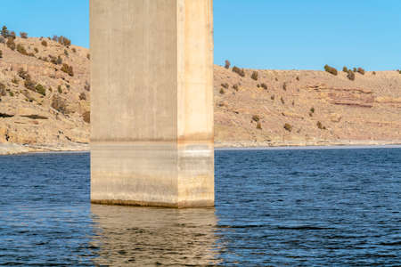 The pier or abutment of a stringer bridge that supports the deck over lake. Rocky slope terrain and cloudy blue sky can be seen in the blurry background.の写真素材